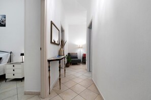 Ein Flur mit einem Bett, einem Nachttisch, einer Lampe und einem kleinen Tisch mit einer Vase und einer Lampe.