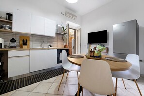 A modern kitchen with white cabinets, a built-in oven, and a dining area with a round table and chairs. - Holiday Home 'Grace’s Garden - Cagliari' (Cagliari)