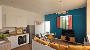 A compact living space with a kitchenette, a dining area, and a seating area with a TV. - Vrbo Property (Thury-Harcourt-le-Hom)
