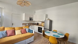 A compact living space with a sofa, a dining table with chairs, a kitchen area, and a ceiling fan. - Vrbo Property (Thury-Harcourt-le-Hom)