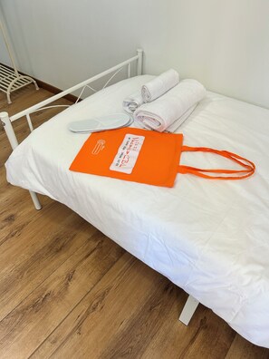 A bed with white bedding, a rolled towel, a white pillow, and an orange bag with text on it.