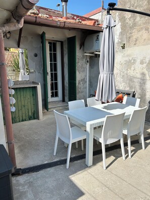 An outdoor patio with a white table and chairs, a grey umbrella, and a green door.