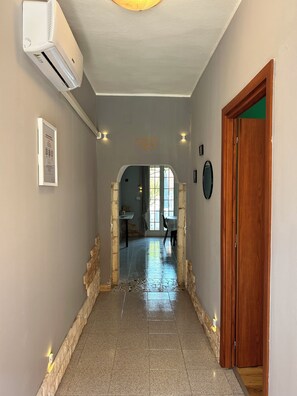 A hallway with a tiled floor, a wooden door, and an air conditioning unit on the wall.