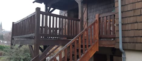 A wooden balcony with a staircase leading to a building entrance.