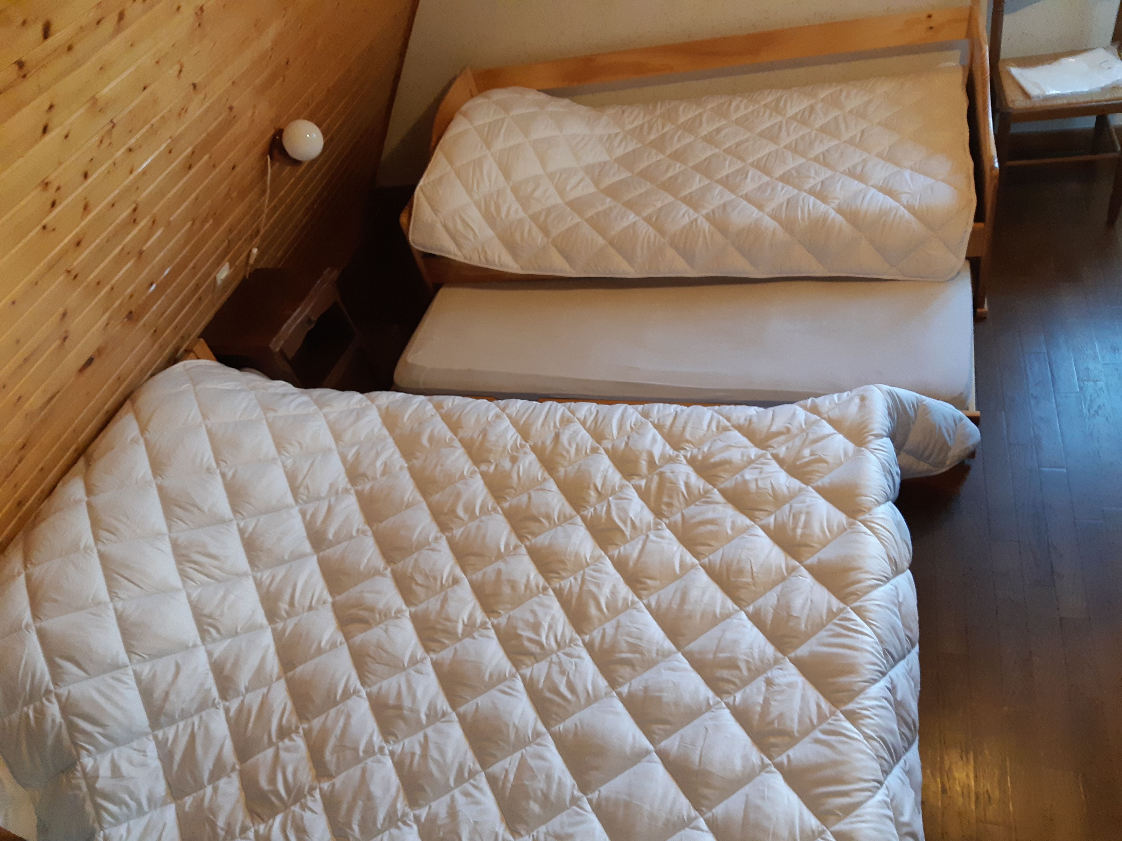 A room with two beds, wooden walls, and a wooden floor.