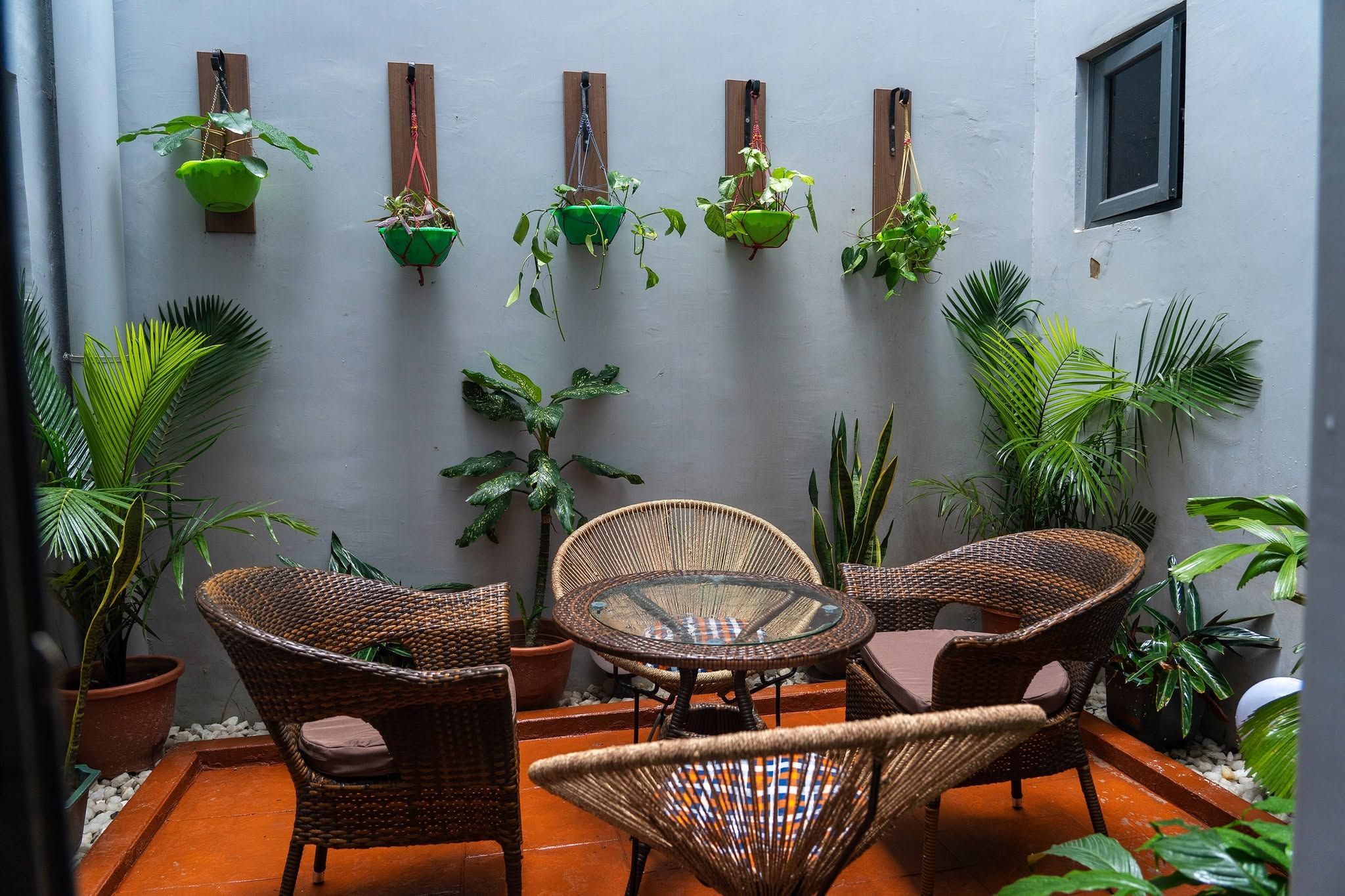 A patio with wicker furniture, a glass table, and various potted plants.