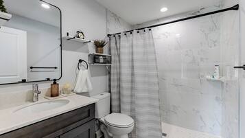 A modern bathroom with a white marble wall, a shower with a grey striped curtain, a white toilet, and a sink with a soap dispenser.