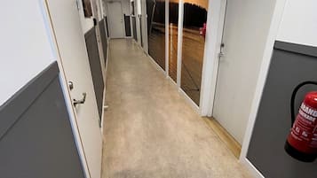 Un couloir avec des portes des deux côtés, un extincteur sur la droite et un panneau de signalisation indiquant la sortie au-dessus.