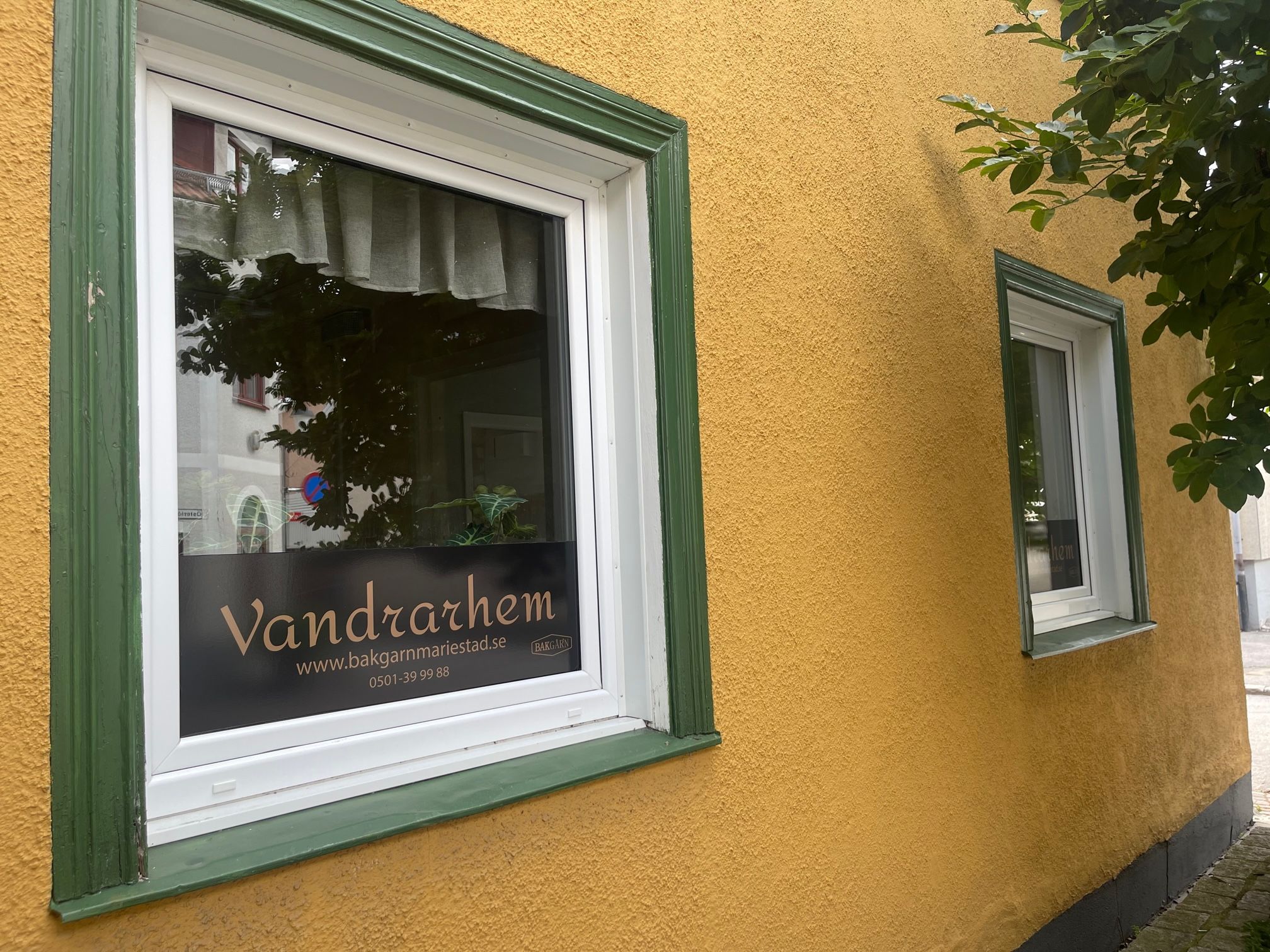 En byggnadsfasad med ett fönster där namnet ”Vandrarhem” och en webbadress visas.