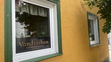 En byggnadsfasad med ett fönster där namnet ”Vandrarhem” och en webbadress visas.