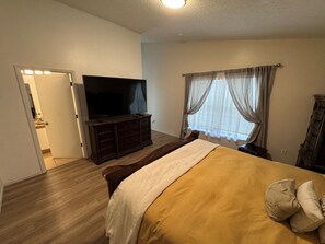 Ein Schlafzimmer mit einem Bett, einem Fernseher, einem Schminktisch und einem Fenster mit Vorhängen.