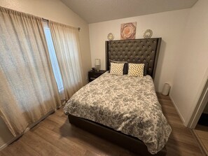 Ein Schlafzimmer mit Bett, Vorhängen, einem Nachttisch und einer Wanddekoration.