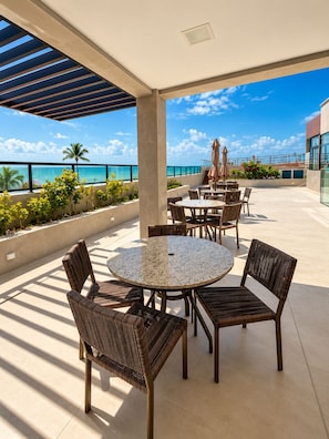 Une terrasse extérieure avec des tables rondes et des chaises en osier, donnant sur une plage.