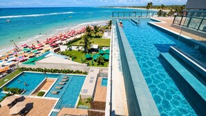 Resort com uma piscina grande, área de praia com guarda-sóis e vista para o oceano.