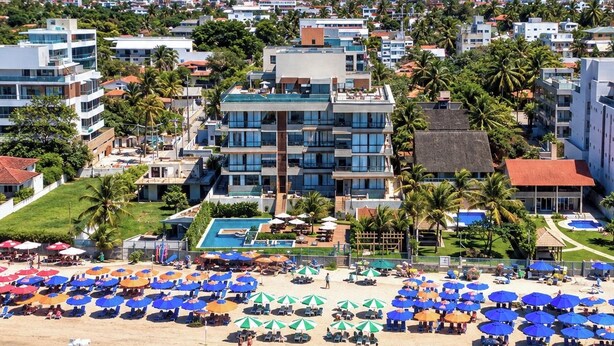 Um resort à beira-mar com piscina, guarda-sóis e um veleiro.