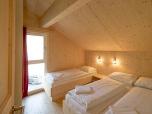 Ein Zimmer mit zwei Einzelbetten, Holzwänden, einer schrägen Decke und einem Fenster mit Blick auf ein Auto vor dem Haus.
