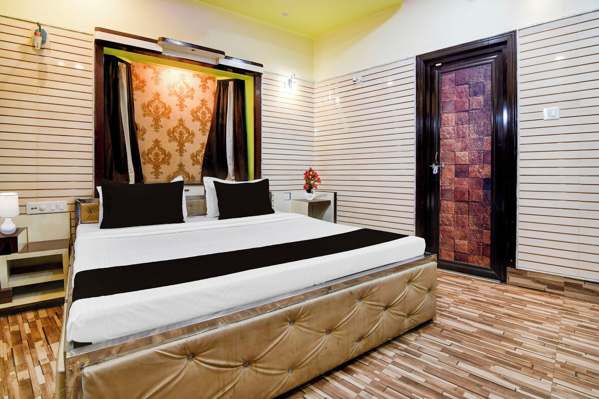 Habitación de hotel con cama, mesitas de noche, una lámpara, un jarrón con flores y una puerta.