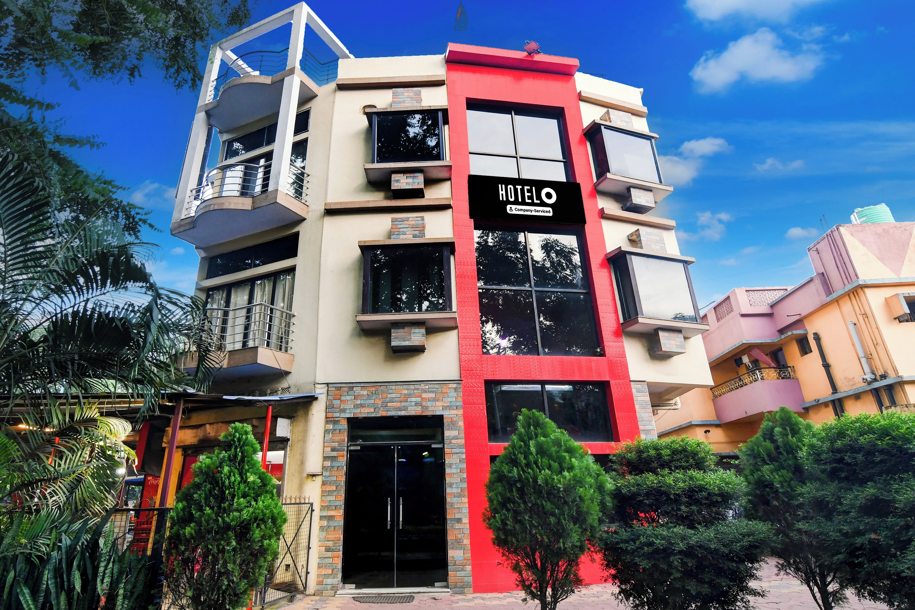 A multi-story hotel with a prominent red and beige facade, a sign indicating it is a company-serviced hotel, and a balcony on the upper floor.