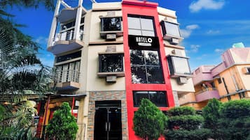 A multi-story hotel with a prominent red and beige facade, a sign indicating it is a company-serviced hotel, and a balcony on the upper floor.