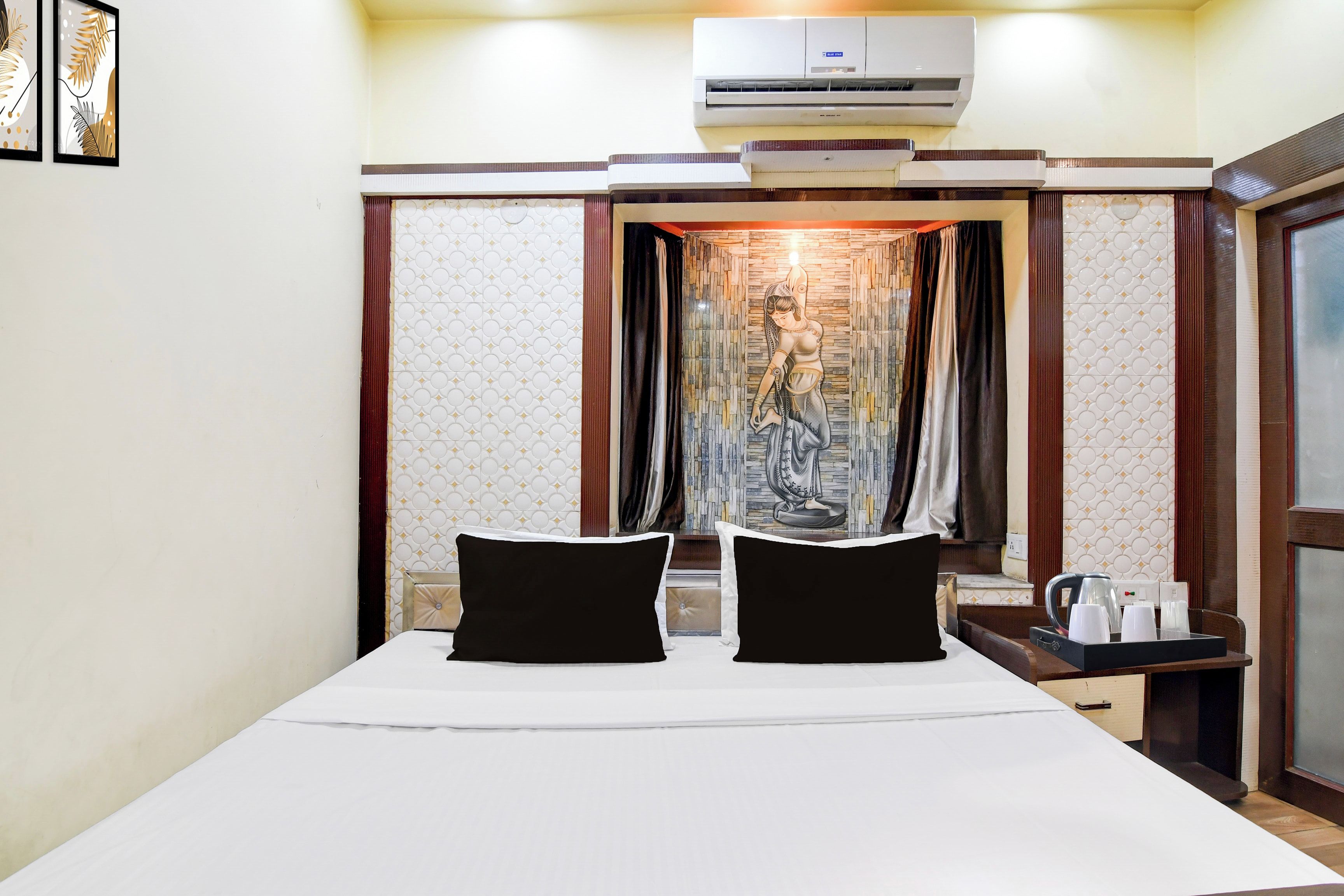 A hotel room with a bed, a nightstand, an air conditioning unit, and a curtain with a painting.