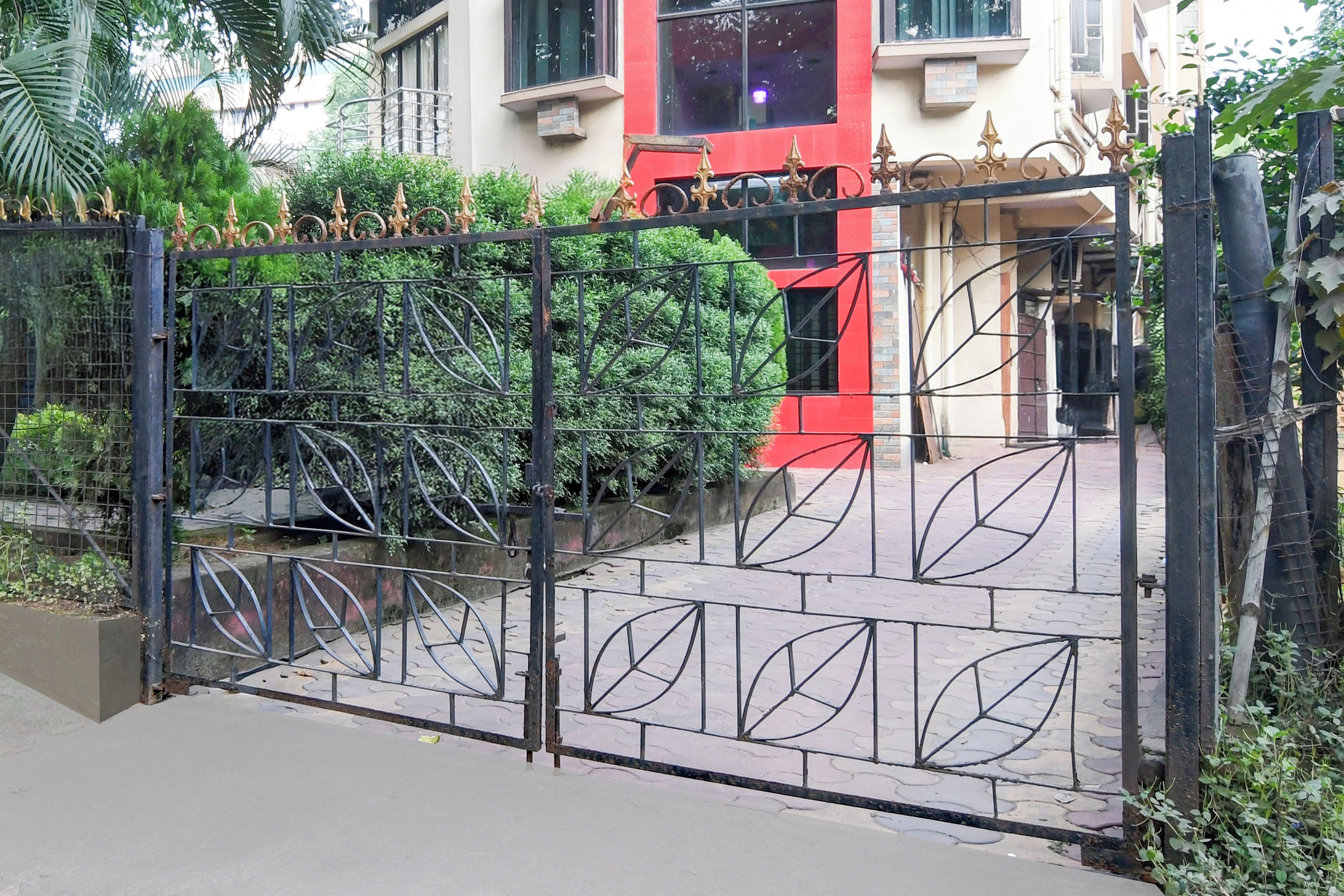 Una entrada protegida por una cerca metálica y un camino pavimentado que conduce a un edificio de fachada roja.