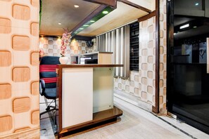 Zona de recepción con mostrador, una silla, un jarrón decorativo y una pared con diseño.