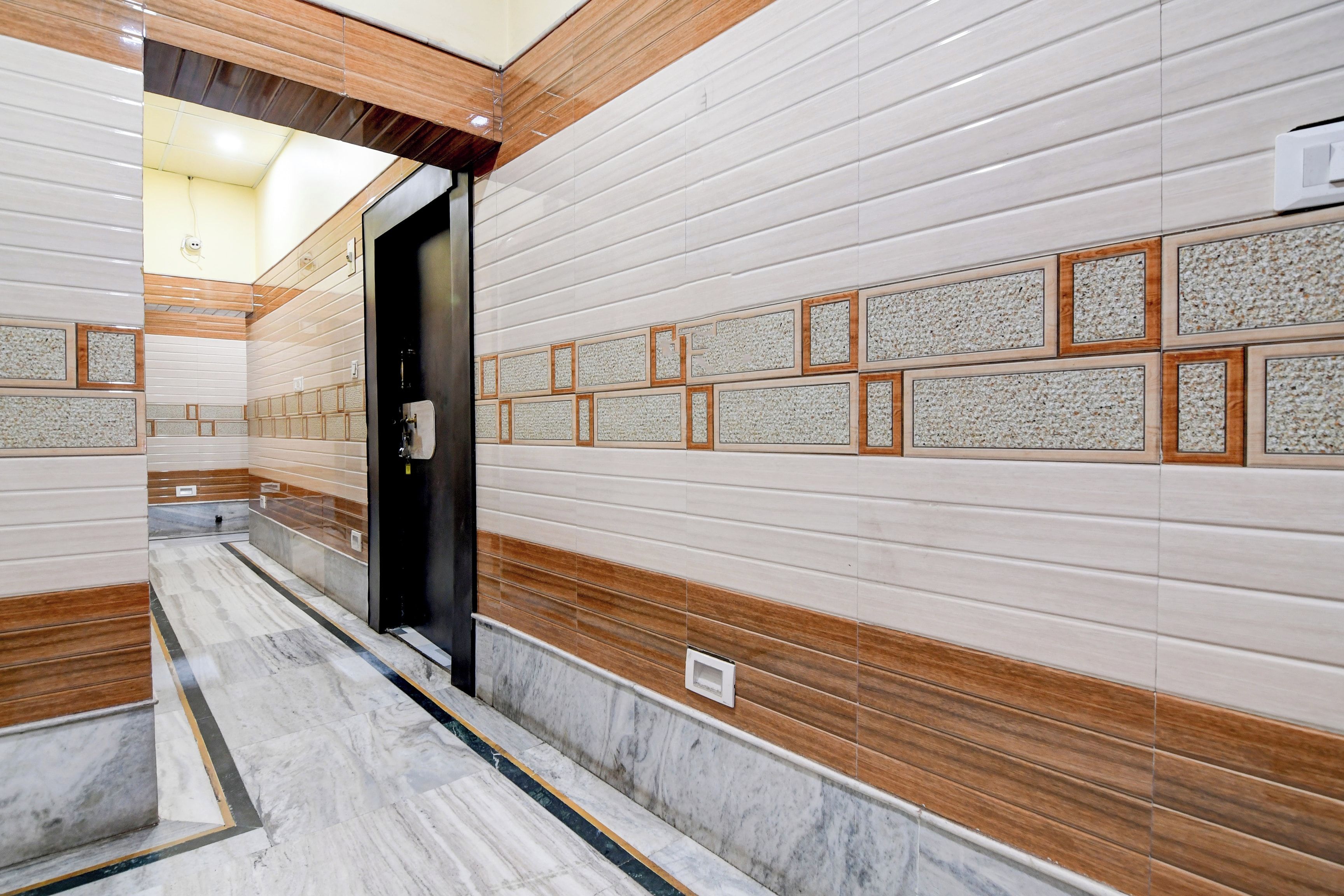 Un pasillo con paredes de azulejos y suelo de mármol, que conduce a una puerta.