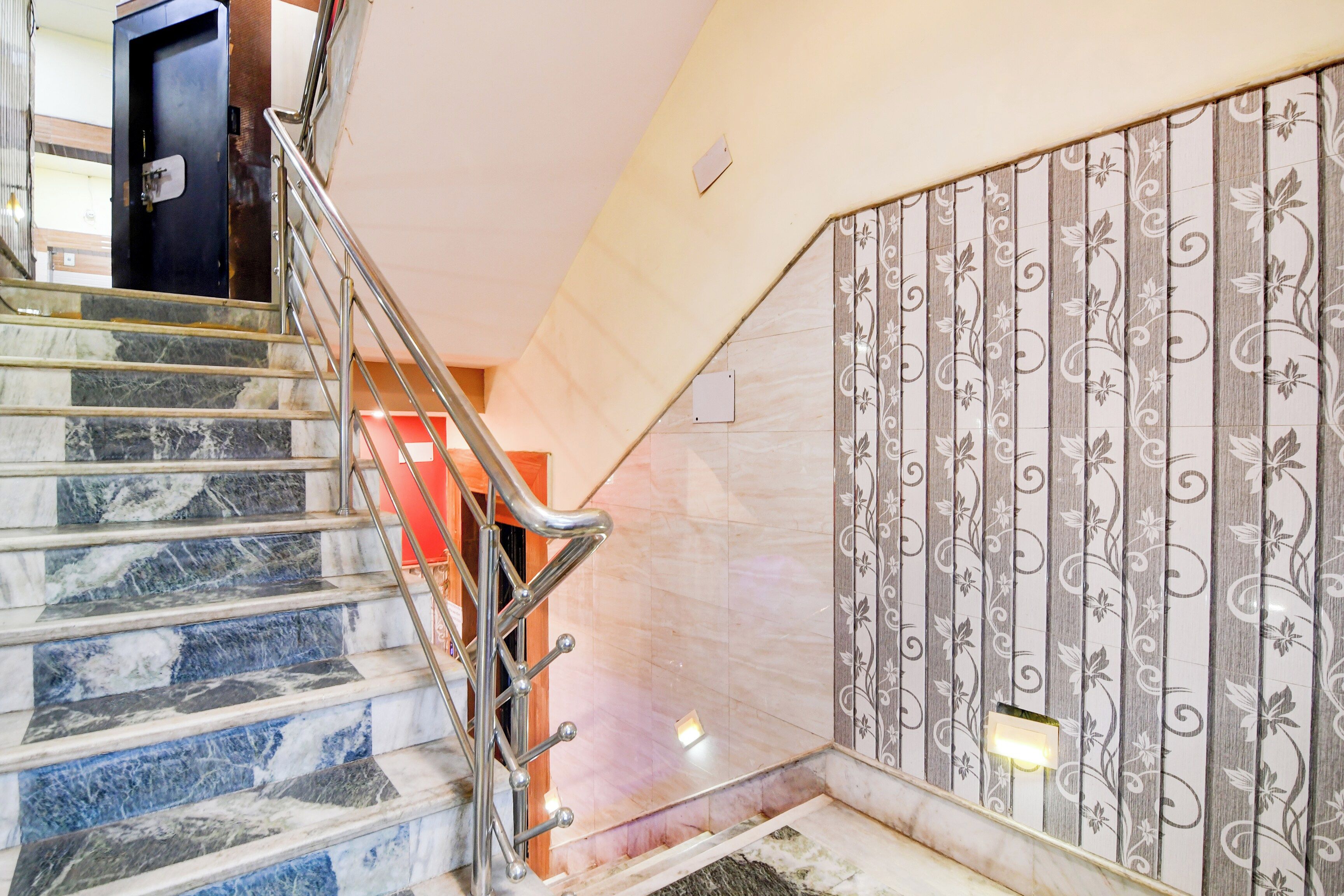 A staircase with marble steps and metal handrails, leading to a room with a patterned wall and a light fixture.