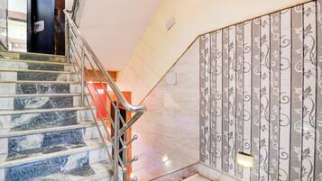 A staircase with marble steps and metal handrails, leading to a room with a patterned wall and a light fixture.