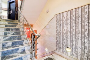 Una escalera con escalones de mármol y barandillas de metal, que conduce a una habitación con un papel tapiz estampado y una lámpara.