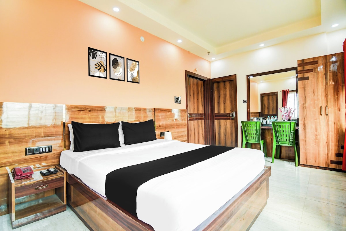 A hotel room with a wooden headboard, a bed with black and white bedding, a nightstand with a phone and a magazine, and a green chair.