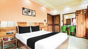 Habitación de hotel con cabecera de madera, cama con ropa de cama blanco y negro, mesita de noche con un teléfono y una revista, y una silla verde.