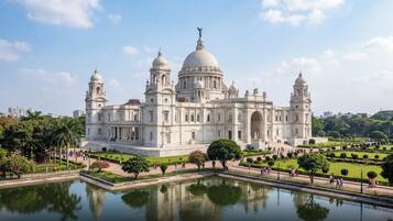 A large, historic building with multiple domes and towers, surrounded by a well-maintained garden and a reflecting pool.