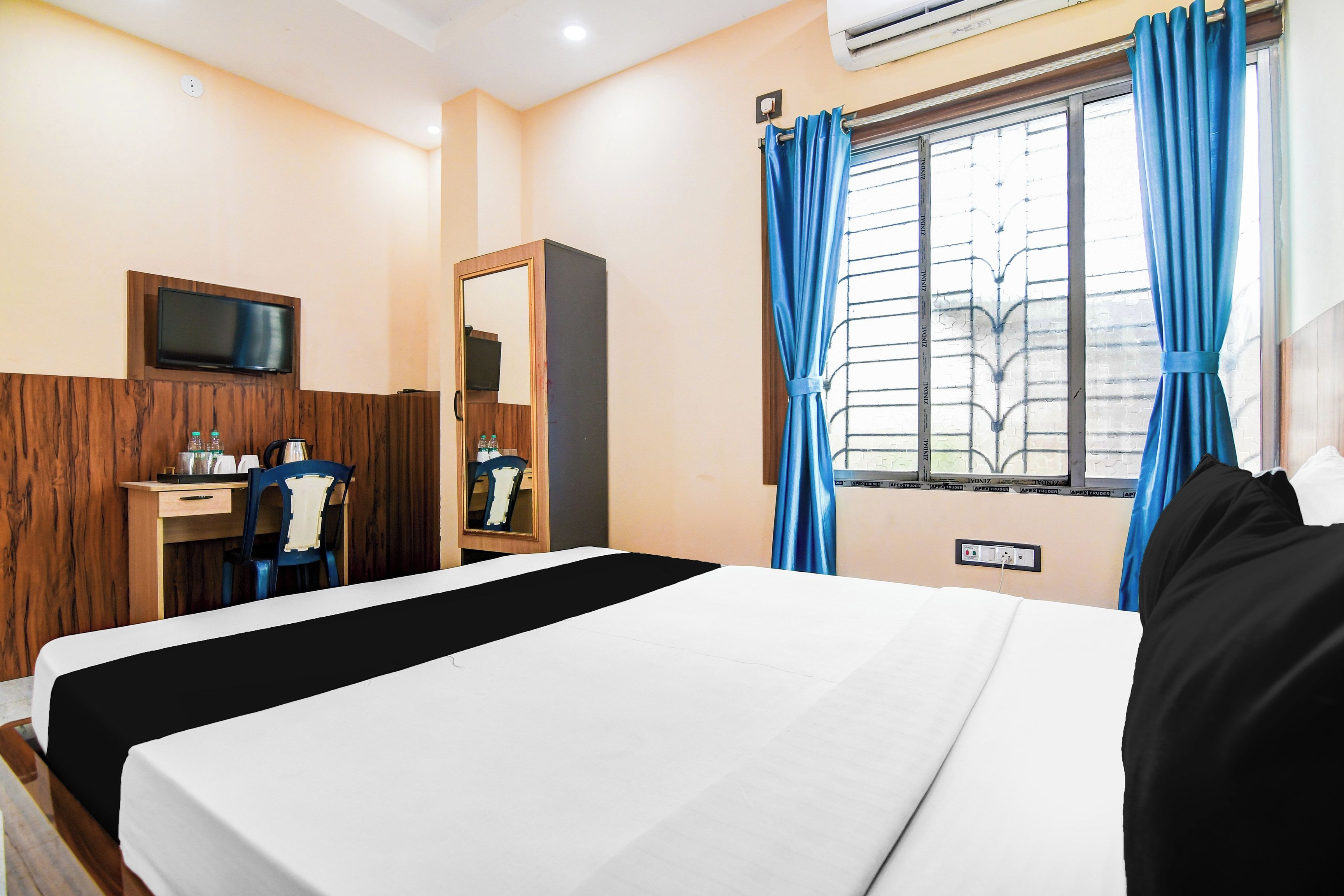 Habitación de hotel con cama, escritorio con silla, televisor montado en la pared y ventana con cortinas.