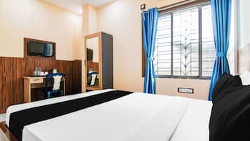 Habitación de hotel con cama, escritorio con silla, televisor montado en la pared y ventana con cortinas.