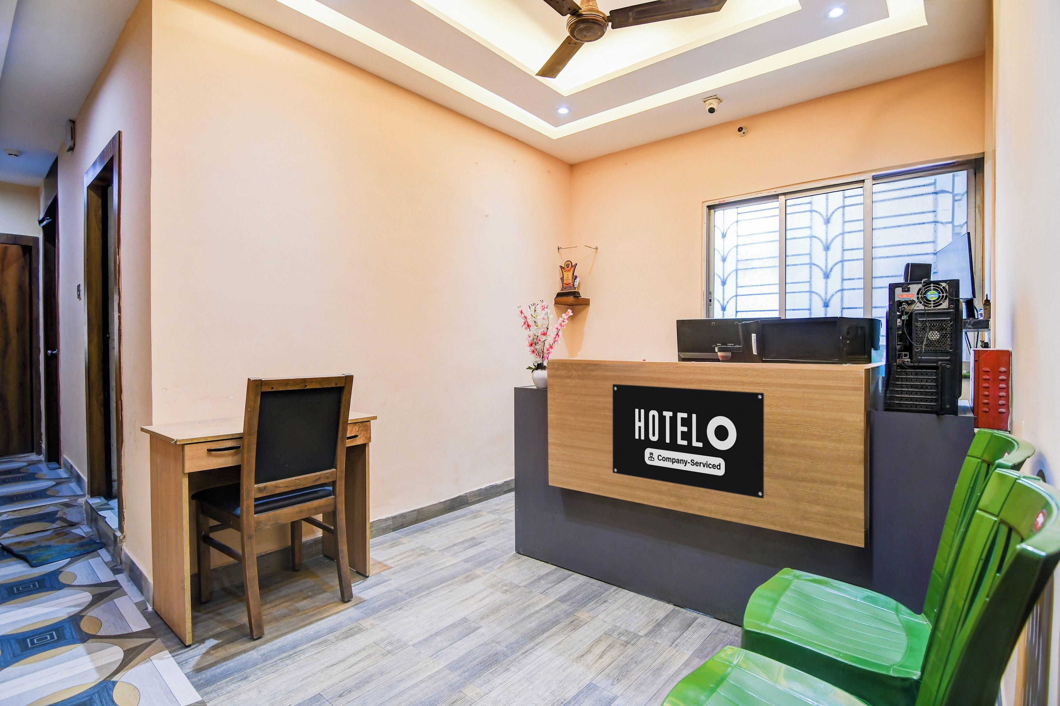 Un mostrador de recepción de hotel con un cartel que indica servicio de empresa, un escritorio con una silla, una ventana con persianas y un ventilador de techo.