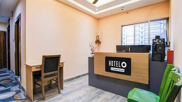 Un mostrador de recepción de hotel con un cartel que indica servicio de empresa, un escritorio con una silla, una ventana con persianas y un ventilador de techo.