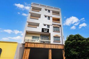 A multi-story hotel with balconies, a sign indicating it is a company-serviced hotel, and a clear blue sky in the background. - Hotel O DumDum Thana More Formerly Bimla (Barakpur)