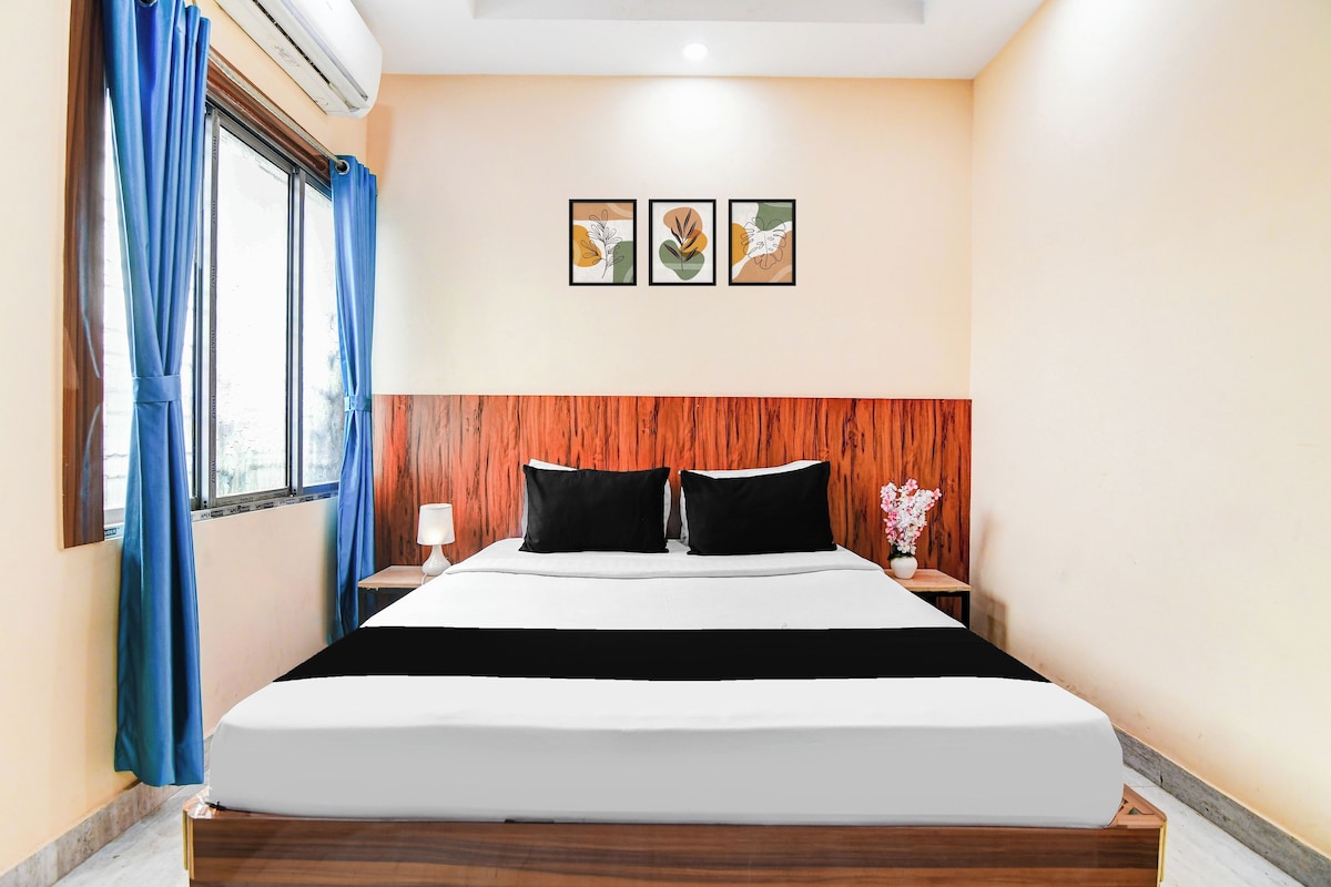 A hotel room with a bed, a nightstand, a lamp, a window with curtains, and three wall-mounted pictures.