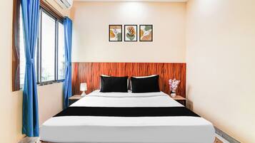 A hotel room with a bed, a nightstand, a lamp, a window with curtains, and three wall-mounted pictures.