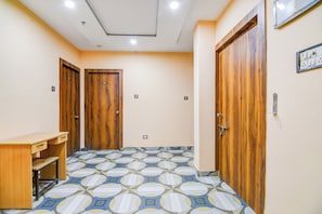A hallway with two wooden doors, a desk, and patterned floor tiles. - Hotel O DumDum Thana More Formerly Bimla (Barakpur)