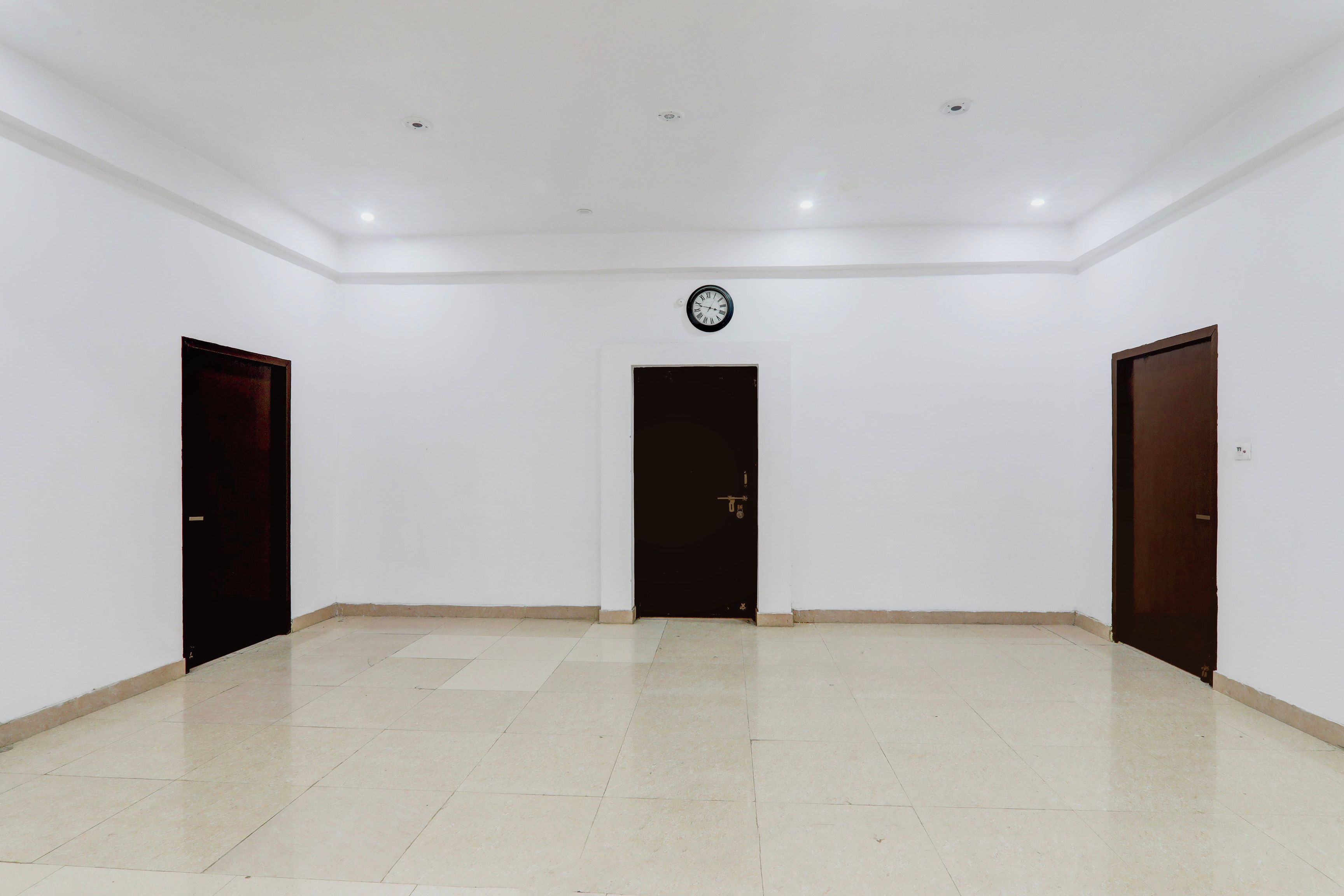 A spacious room with a tiled floor, three doors, and a clock on the wall.