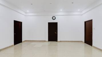 A spacious room with a tiled floor, three doors, and a clock on the wall.