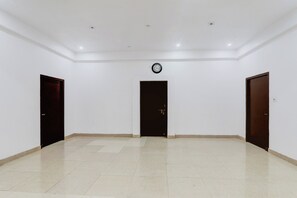 A spacious room with a tiled floor, three doors, and a clock on the wall.