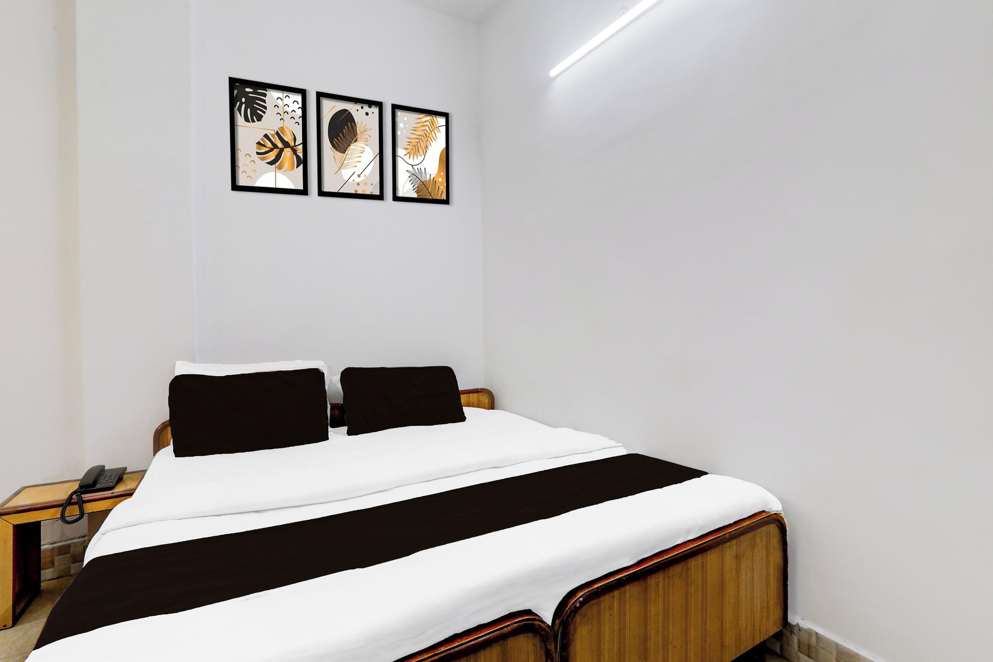 Hotellihuone, jossa on sänky, kaksi yöpöytää ja seinällä kolme kehystettyä taideteosta.