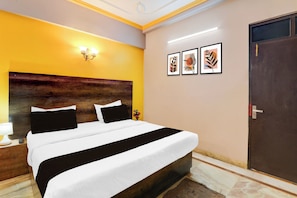 Habitació d'hotel amb un llit gran, un panell de capçal de fusta, una tauleta de nit amb una làmpada i una porta.