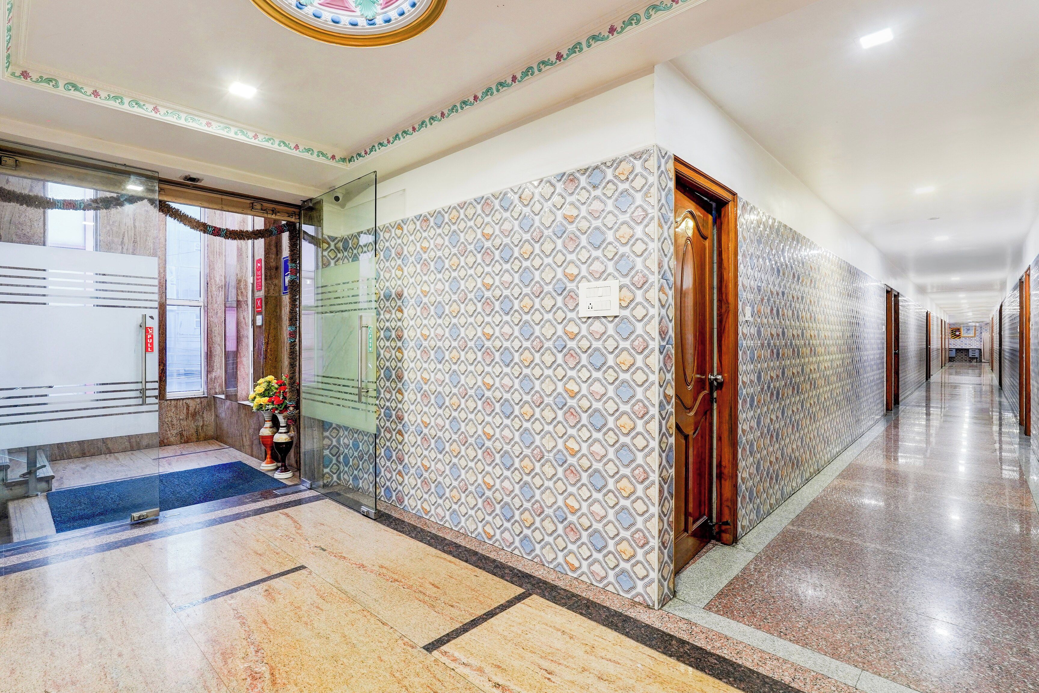 Un pasillo de hotel con paredes estampadas, piso de mármol y puerta de madera.