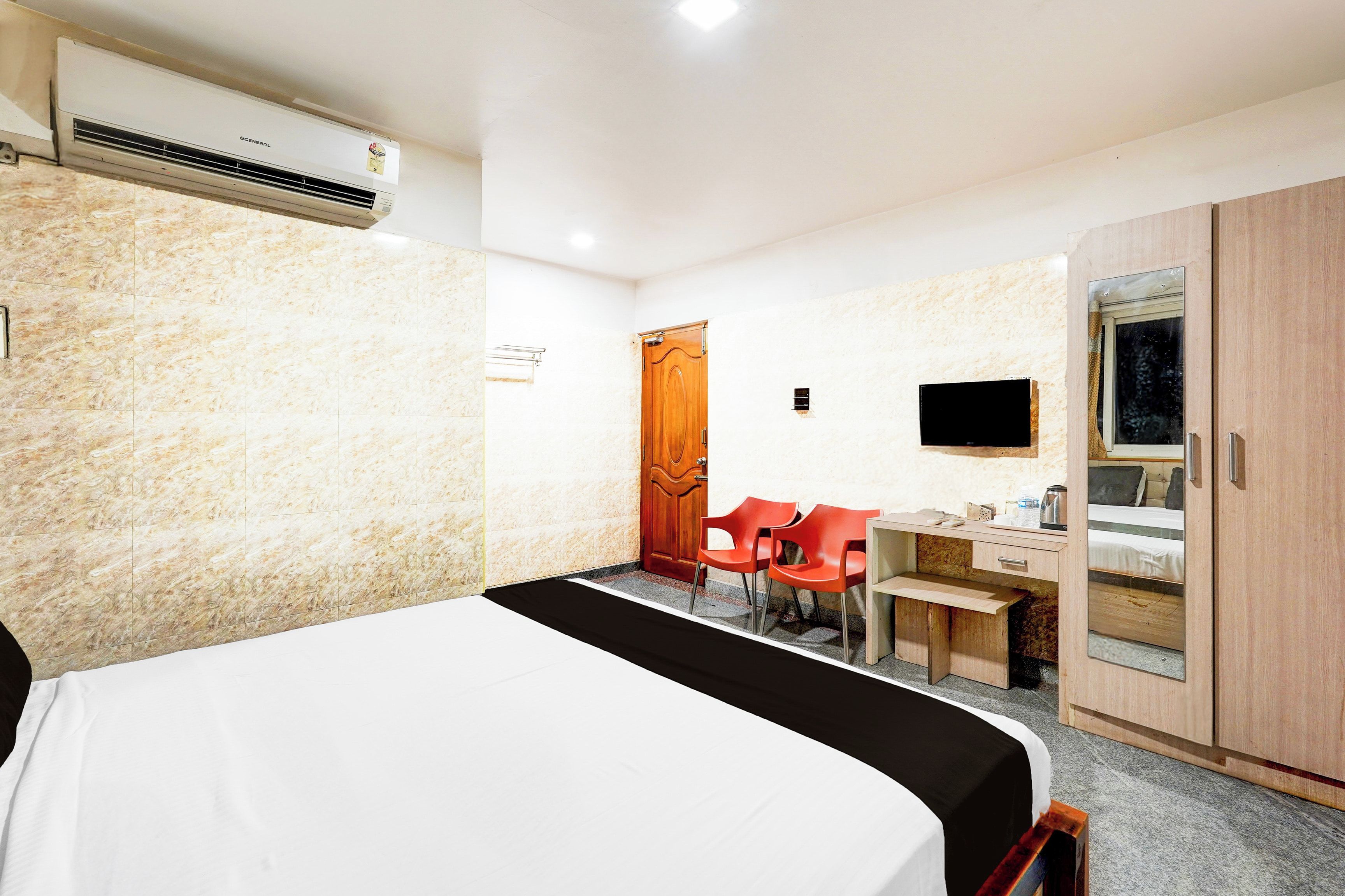 Una habitación de hotel con cama, escritorio, silla, televisor y armario.