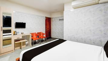 A hotel room with a bed, a desk, two chairs, a TV, and an air conditioning unit.