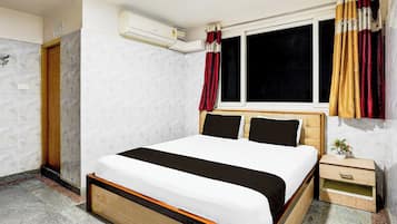 Habitación de hotel con cama, ventana con cortinas, unidad de aire acondicionado y una mesita de noche con una planta.